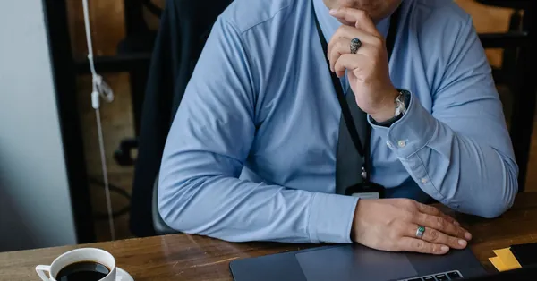 From above of crop adult male business owner thinking on problem while working on netbook in office serious businessman touching chin while working on laptop