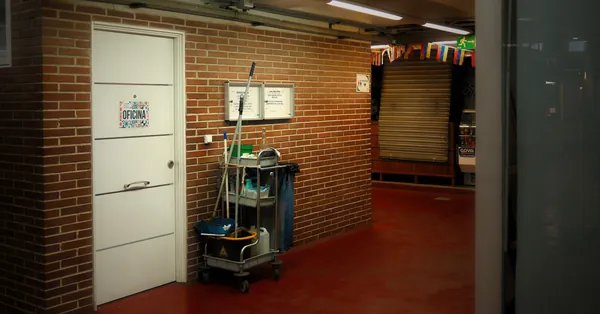 A brightly lit industrial hallway with a cleaning cart and supplies near an office door. industrial hallway with cleaning cart setup