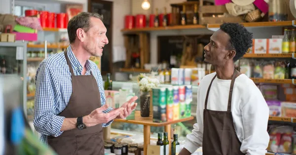 Two colleagues in aprons conversing in a grocery store setting. men talking inside a grocery store