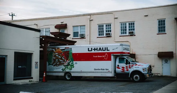 A U-Haul moving truck parked in front of a beige warehouse building. truck parked by warehouse