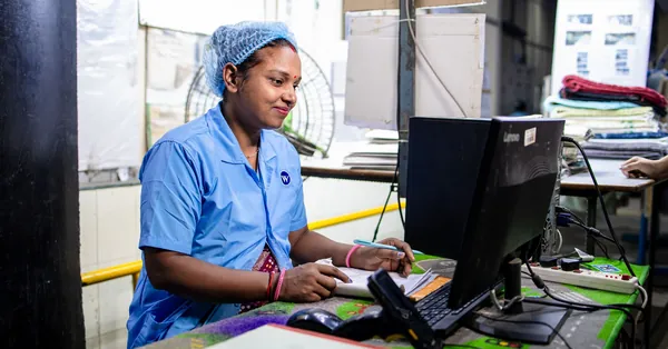 Female factory worker inputs data in a textile manufacturing setting. Indoors and focused. textile factory worker at computer station