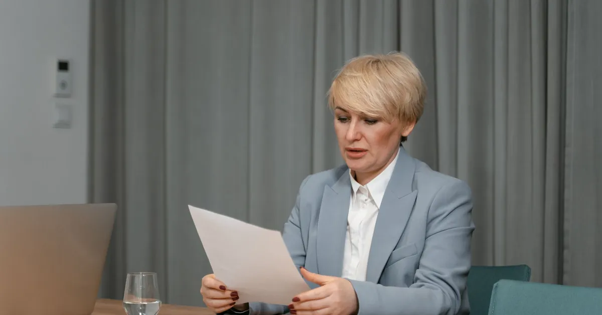Businesswoman in a blazer reviewing documents at a desk. Professional office setting with laptop and papers. a woman sitting at a desk looking at paperwork