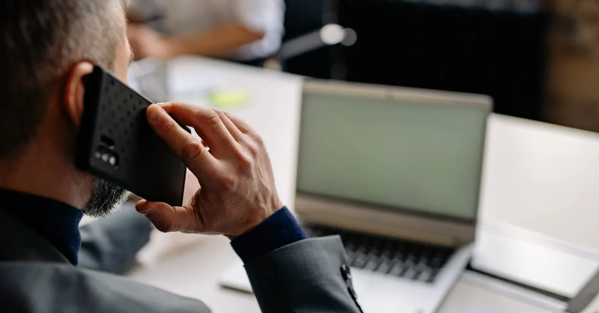Professional man using cellphone in office setting, multitasking with a laptop. a man having a phone call while working on his computer