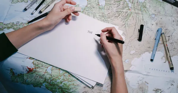 Hands writing on paper over a detailed world map with various pens. a person writing on a piece of paper