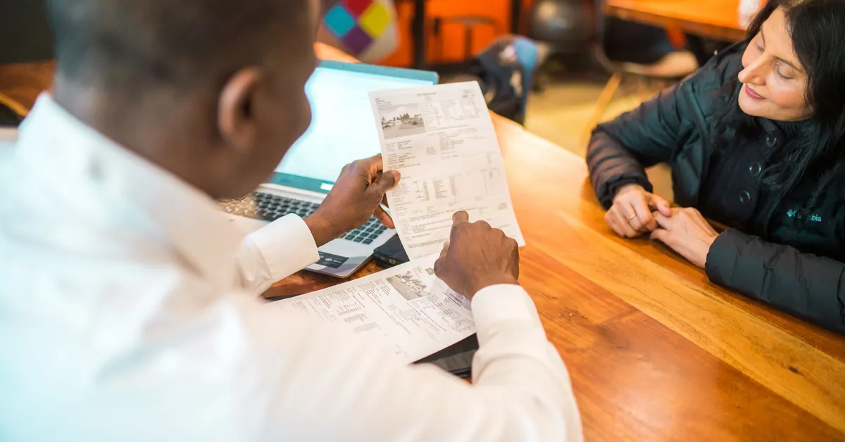 Two adults discussing documents in a business setting indoors. a man and woman holding a paper