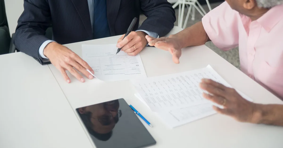 A business meeting between an elderly client and a consultant discussing documents at an office table. an elderly man consulting an insurance agent