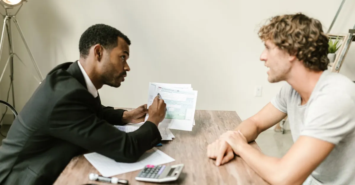 A financial advisor discusses paperwork with a client at a desk in a modern office. an agent showing documents to his client