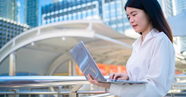 Confident Asian businesswoman working on laptop outdoors in Bangkok, symbolizing modern entrepreneurship. asian businesswoman working on laptop outdoors