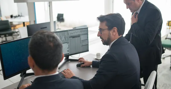 Colleagues in a modern office reviewing stock market trends and data on multiple screens. men using computer in a office