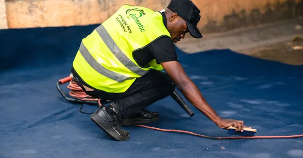 A worker dressed in a safety vest cleans a blue carpet outdoors with a brush. worker cleaning carpet with brush in outdoor setting