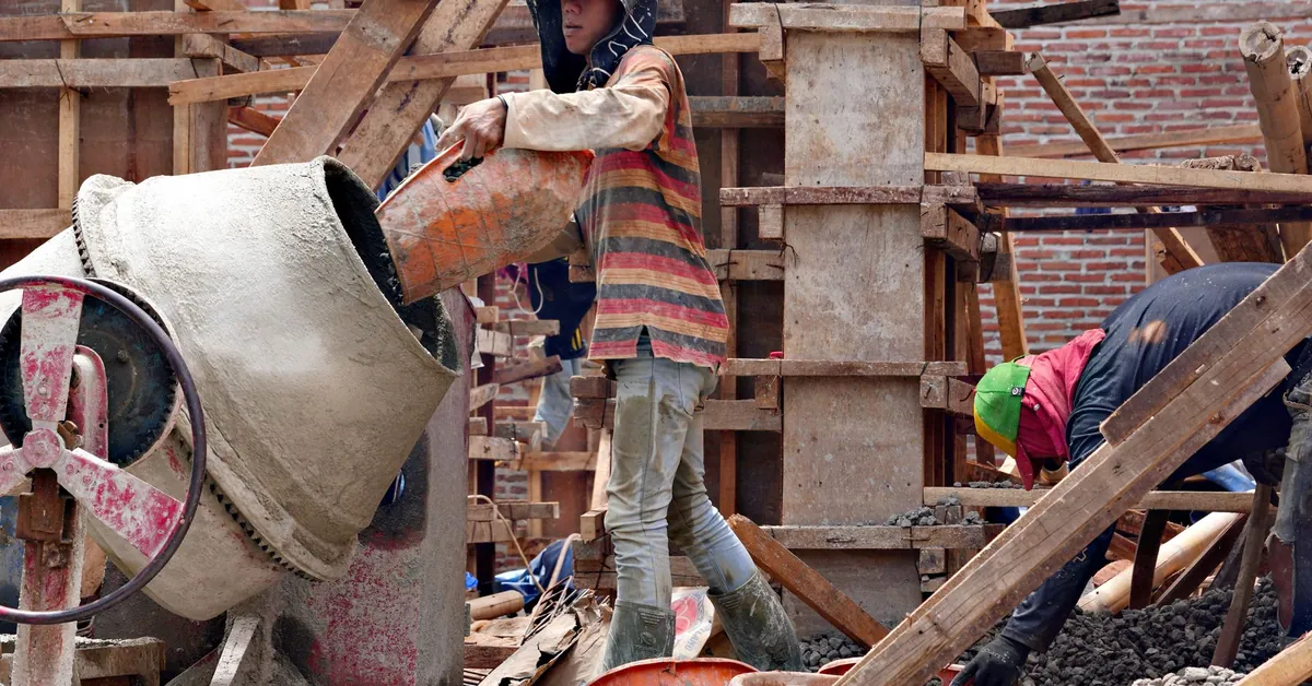 Construction workers mixing cement at a building site. Manual labor in progress with wooden scaffolding. construction workers operating cement mixer at site