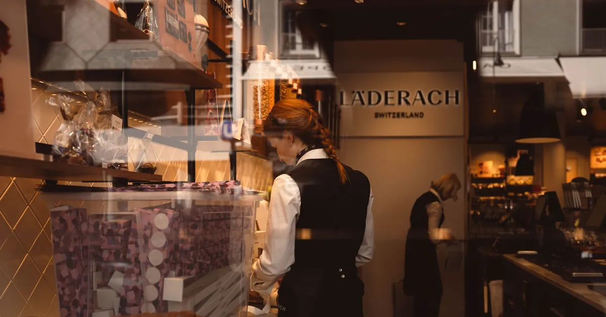View through a shop window of Läderach store in Switzerland, showcasing employees working. chocolate shop interior with two female employees