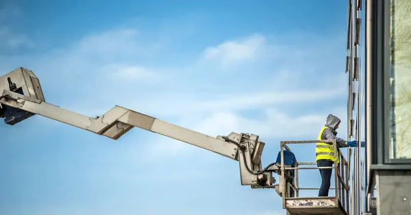 A construction worker cleans glass windows on a high-rise building using an industrial lift. man working high in industrial basket