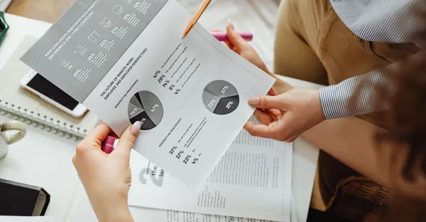 Two people reviewing financial reports and graphs at a desk for analysis and decision-making. close up photo of accounting documents