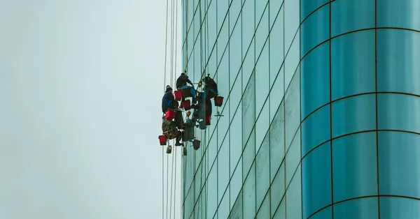 Window cleaners suspended on ropes working on a tall glass building facade. people cleaning the exterior of a building