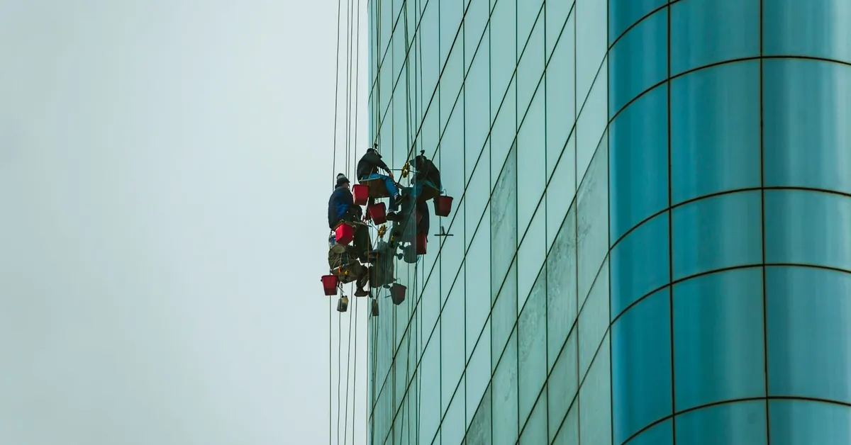 Window cleaners suspended on ropes working on a tall glass building facade. people cleaning the exterior of a building