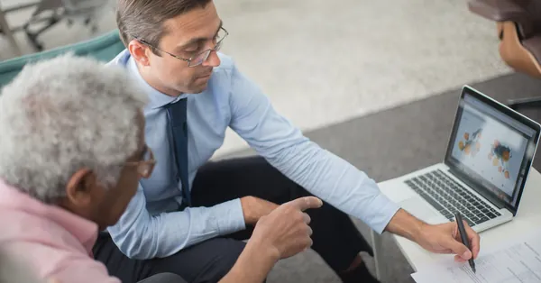 Two men in a business meeting reviewing financial documents and discussing data on a laptop. two men looking the document