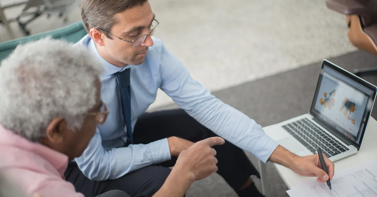 Two men in a business meeting reviewing financial documents and discussing data on a laptop. two men looking the document
